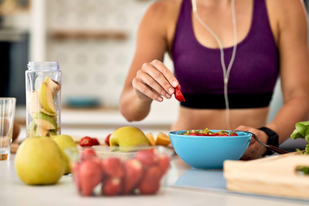 Mulher atlética preparando uma salada de frutas na cozinha. Uma representação visual do equilíbrio entre nutrição esportiva e atividade física para uma vida saudável.