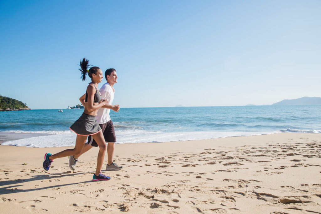 Casal praticando corrida na praia, promovendo hábitos saudáveis e um estilo de vida equilibrado.