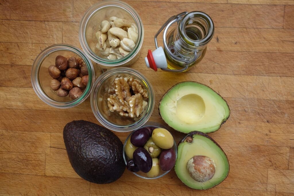 Diversas fontes de gorduras saudáveis, como azeite de oliva, abacates, nozes e castanhas, dispostas sobre uma mesa de madeira.