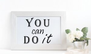 Porta-retrato branco com a frase 'You can do it' ('Você consegue'), acompanhado por um vaso de flores brancas, símbolo de renovação e crescimento.