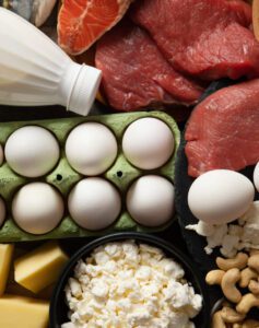 Diversidade de fontes proteicas: carne vermelha, peixe, ovos, leite, queijos e castanhas dispostos sobre uma mesa, representando uma ‘Alimentação Equilibrada’ com diferentes fontes de proteína.