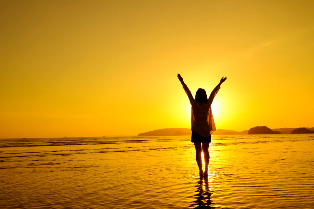 Silhueta de uma mulher na praia admirando o nascer do sol, representando uma rotina matinal saudável e energizante.