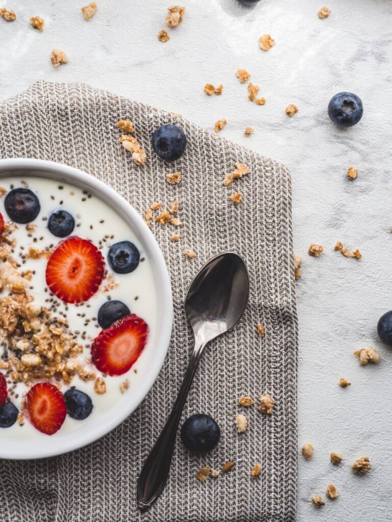 Imagem de uma tigela repleta de Iogurte Natural com granola, morangos e blueberries, proporcionando uma experiência saudável e deliciosa. Ideal para a jornada de emagrecimento.