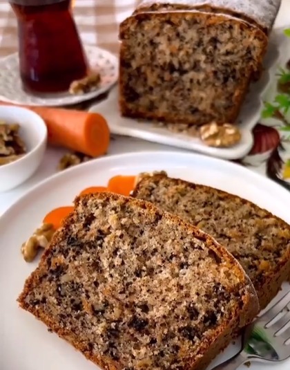 Imagem de um Bolo de Nozes, Cenoura e Chocolate em uma travessa, destacando a suculência da fatia servida em um prato com rodelas de cenoura e nozes ao lado. Uma celebração equilibrada e deliciosa.