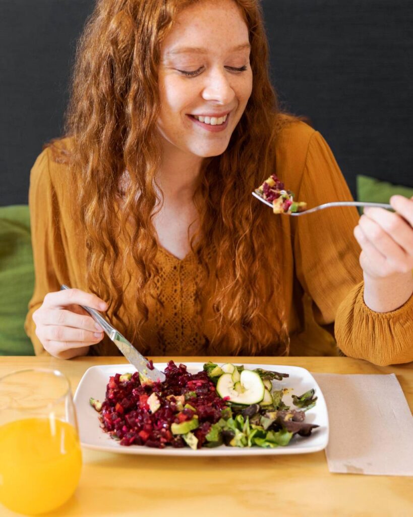 Mulher sorridente prestes a saborear uma salada fresca à mesa, representando a prática de Mindful Eating e apreciação consciente dos alimentos.