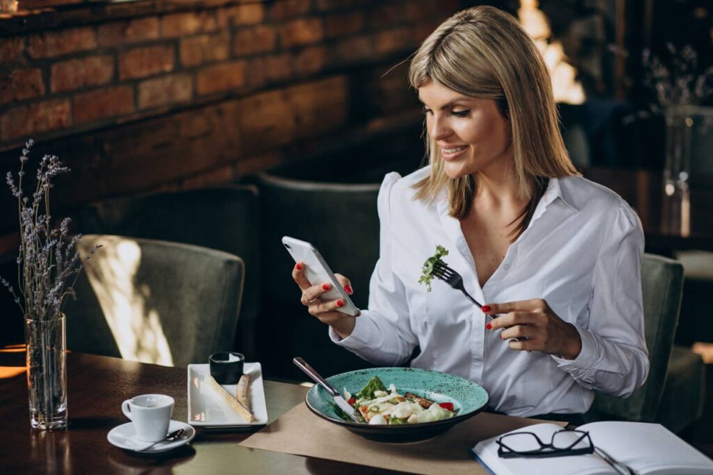 Imagem de uma mulher ocupada desfrutando de uma refeição saudável em um restaurante, representando o conceito de 'Alimentação Inteligente' na rotina diária.