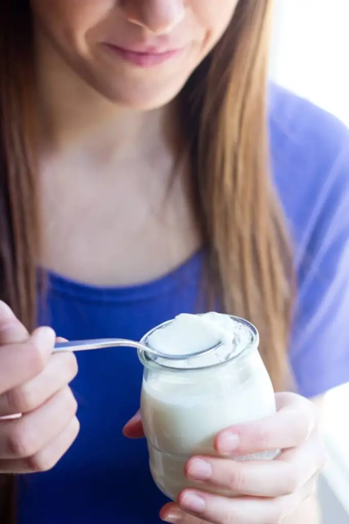 Mulher sorridente segurando um copo de iogurte natural, destacando a importância dos probióticos na saúde digestiva.