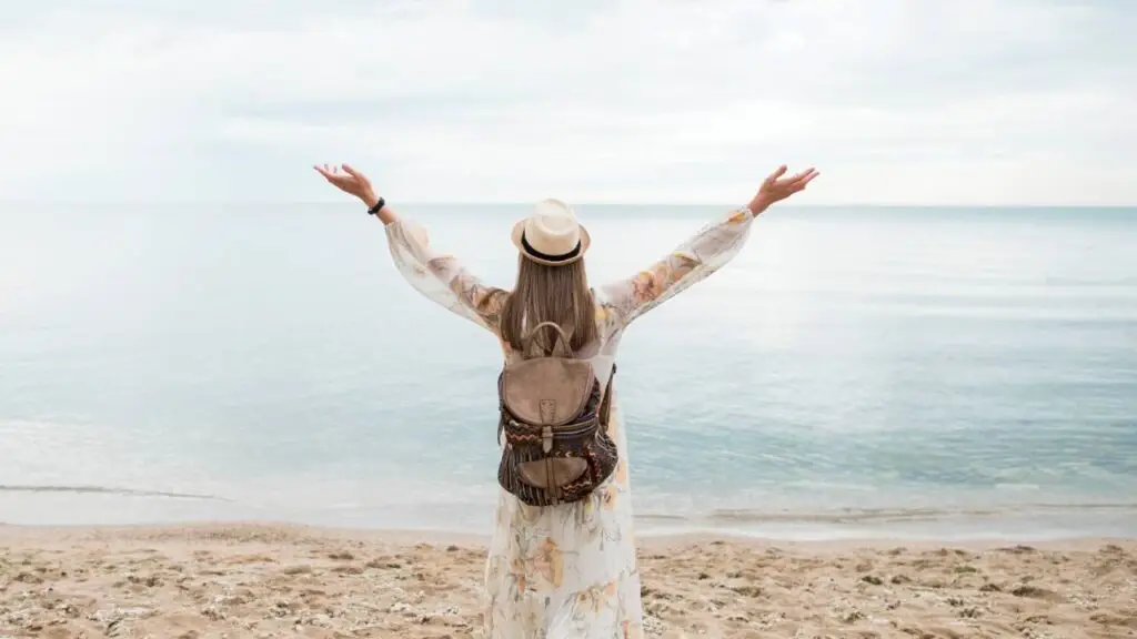 Mulher de braços abertos em uma praia tranquila, representando o impacto positivo da gratidão diária na saúde e bem-estar.