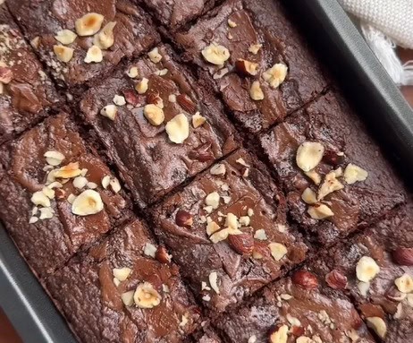 Brownie funcional saudável, com cobertura de creme de avelã, pedaços de chocolate 70% e avelãs trituradas, pronto para ser servido.