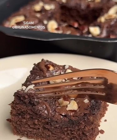 Brownie funcional saudável servido em um prato, com cobertura de creme de avelã, pedaços de chocolate 70% e avelãs trituradas.