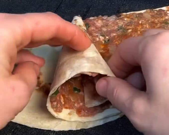 Imagem da tortilha com carne moída sendo dobrada em forma de cone.