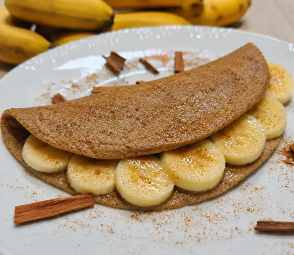 Imagem de uma deliciosa crepioca de banana sobre uma mesa, recheada de rodelas de banana e salpicada com canela, destacando o equilíbrio entre sabor e nutrição.